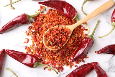 Photo of Chili pepper flakes and pods on white marble table, flat lay