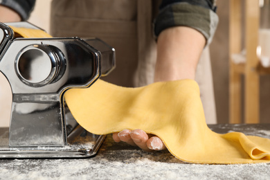 Woman preparing dough with pasta maker machine at table, closeup