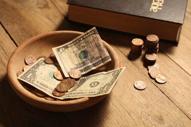 Photo of Donate and give concept. Coins, dollar banknotes and Bible on wooden table, closeup
