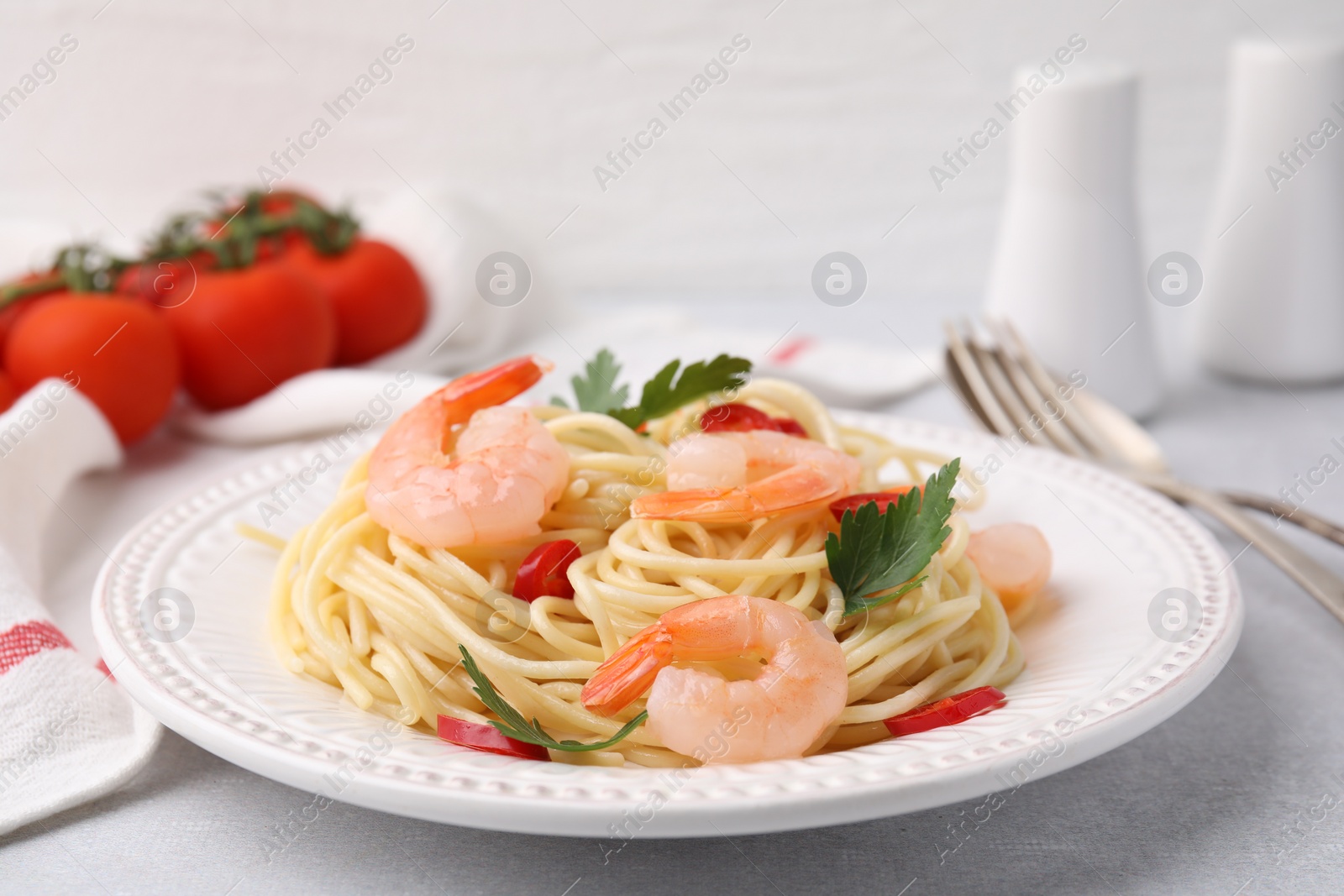 Photo of Tasty spaghetti with shrimps, chili pepper and parsley on grey table, closeup