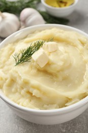 Photo of Bowl of delicious mashed potato with dill and butter on light grey table, closeup