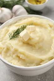 Bowl of delicious mashed potato with dill and butter on light grey table, closeup