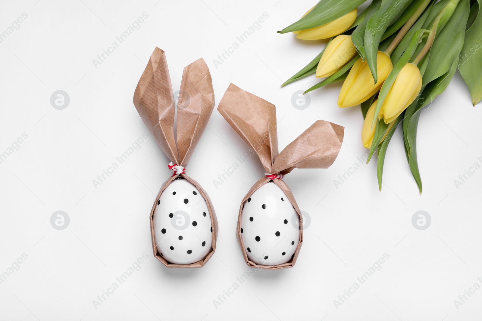 Photo of Easter bunnies made of craft paper and eggs near beautiful tulips on white background, flat lay