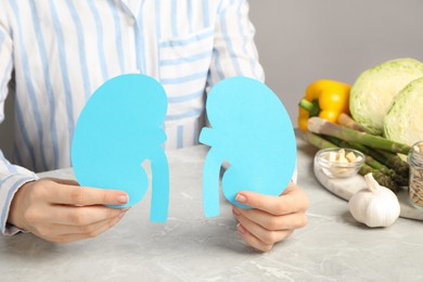 Photo of Woman holding paper cutout of kidneys near different products on grey table, closeup