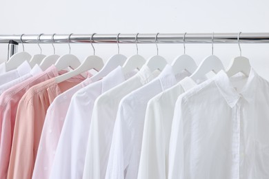 Photo of Rack with different stylish shirts near white wall, closeup. Organizing clothes