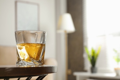 Photo of Glass of whiskey on wooden table in modern room interior, space for text