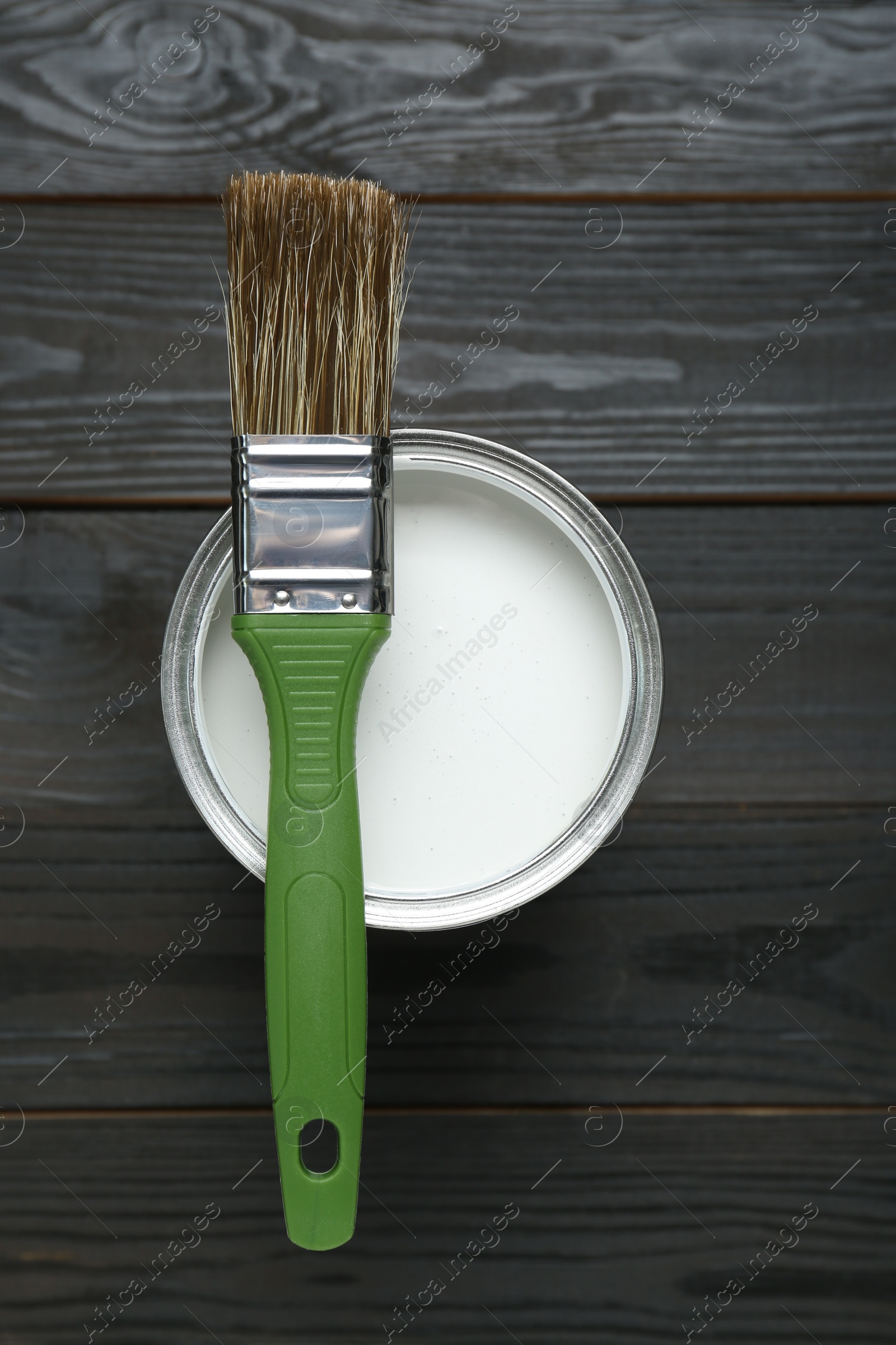 Photo of Can of white paint with brush on black wooden table, top view