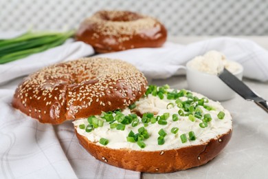 Photo of Delicious bagel with cream cheese and green onion on light table, closeup