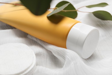 Tube of face cleansing product, cotton pads and leaves on white fabric, closeup