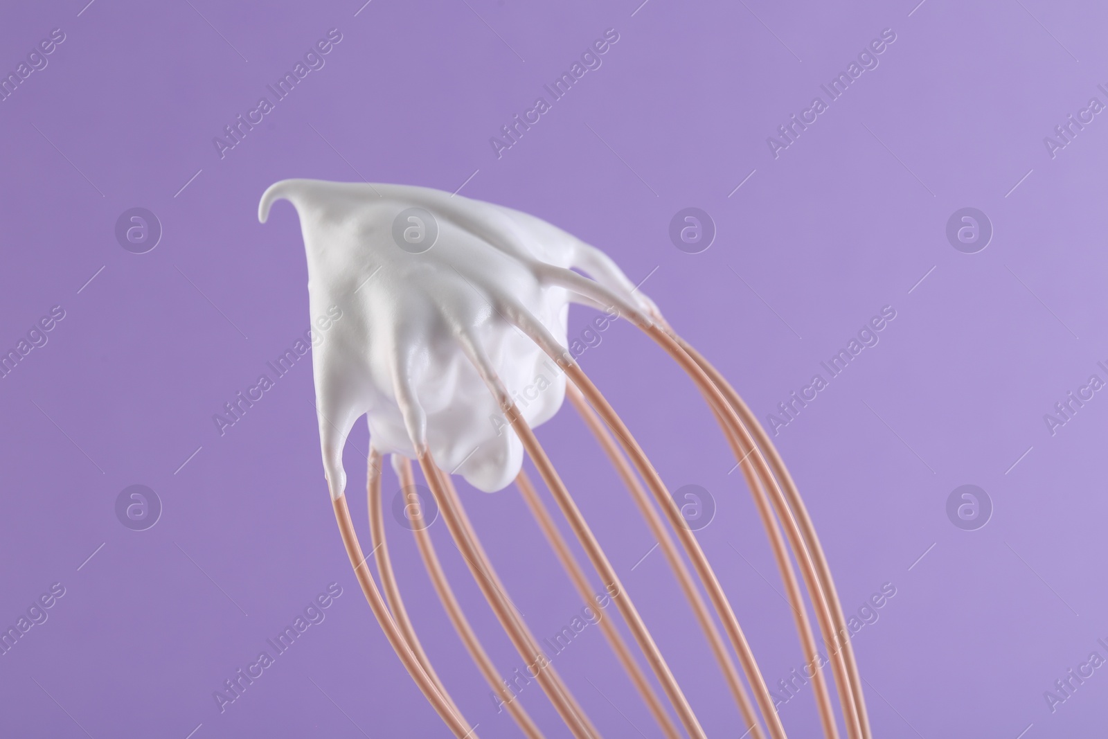 Photo of Whisk with whipped cream on violet background, closeup