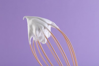 Photo of Whisk with whipped cream on violet background, closeup