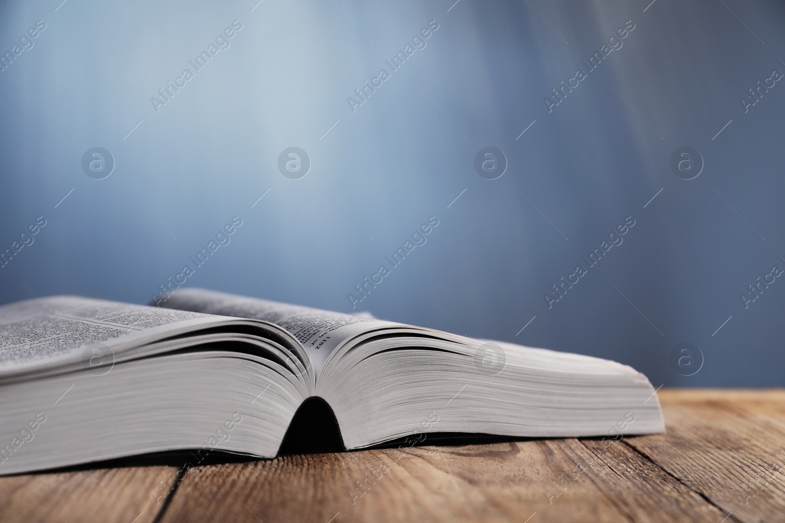 Photo of Closeup view of open Bible on wooden table against grey background, space for text. Religious book