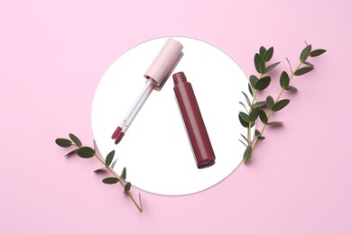 Photo of Lip gloss, green twigs and mirror on pink background, flat lay