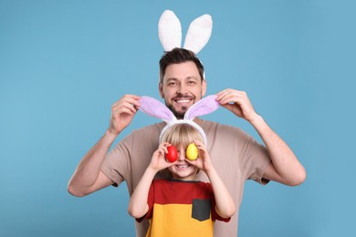 Photo of Father and son in bunny ears headbands having fun on turquoise background. Easter celebration