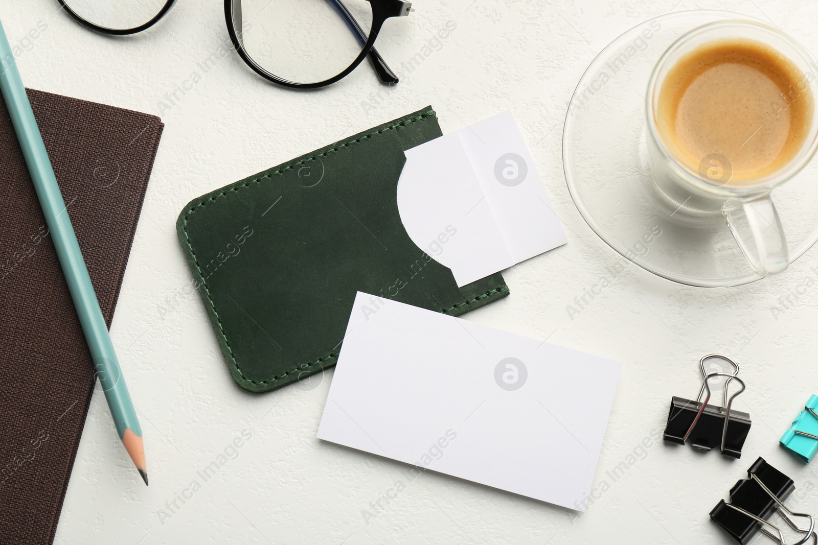 Photo of Leather business card holder with blank cards, glasses, coffee and stationery on white table, flat lay