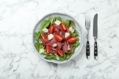 Photo of Delicious bresaola salad with tomatoes and parmesan cheese served on white marble table, flat lay