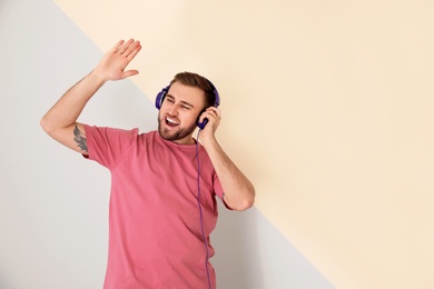 Photo of Handsome man enjoying music in headphones on color background. Space for text