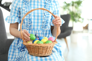 Beautiful woman holding basket with Easter eggs at home, closeup. Space for text