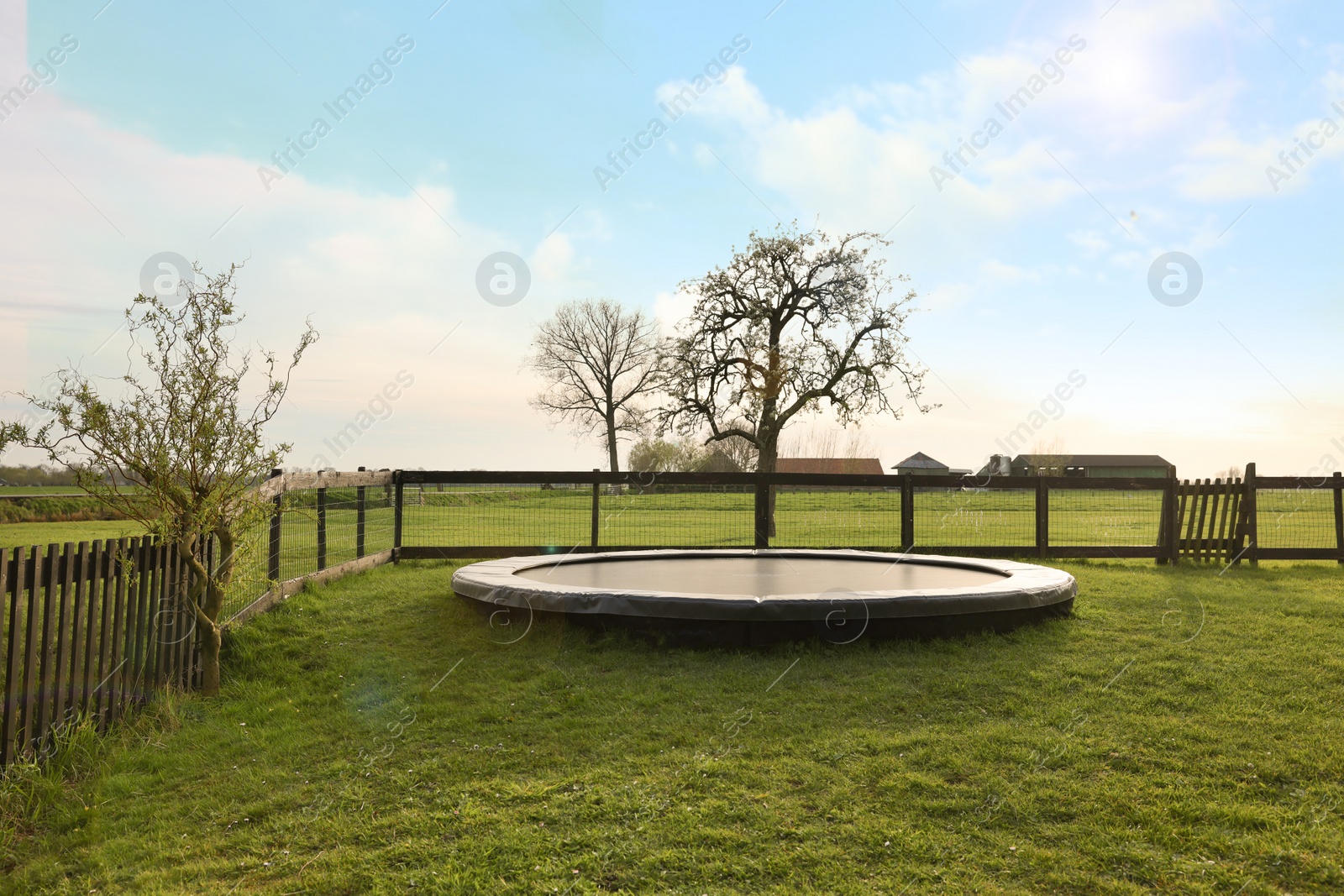 Photo of Big trampoline near wooden fence on green lawn outdoors