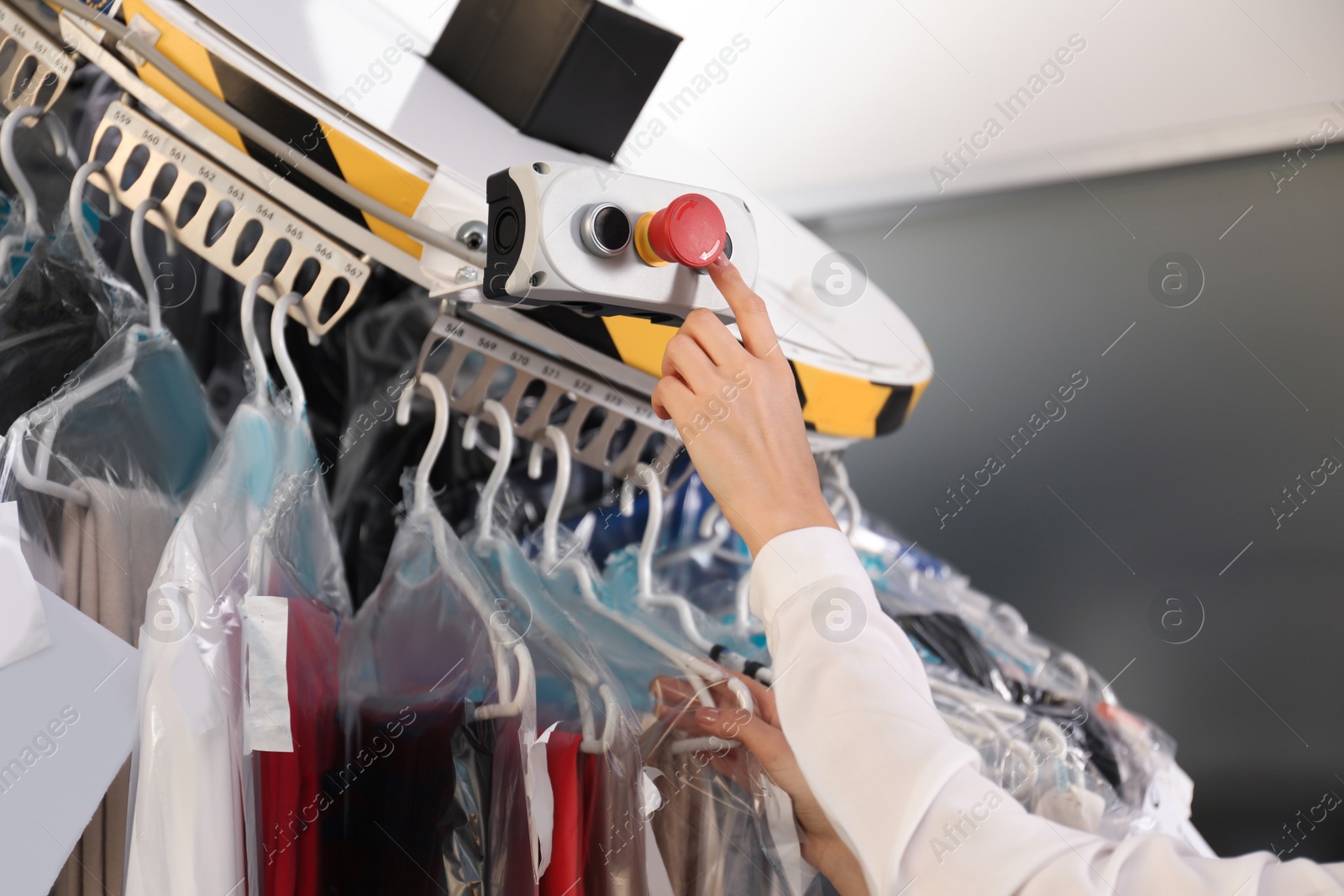Photo of Worker pressing button on control panel of garment conveyor at modern dry-cleaner's, closeup