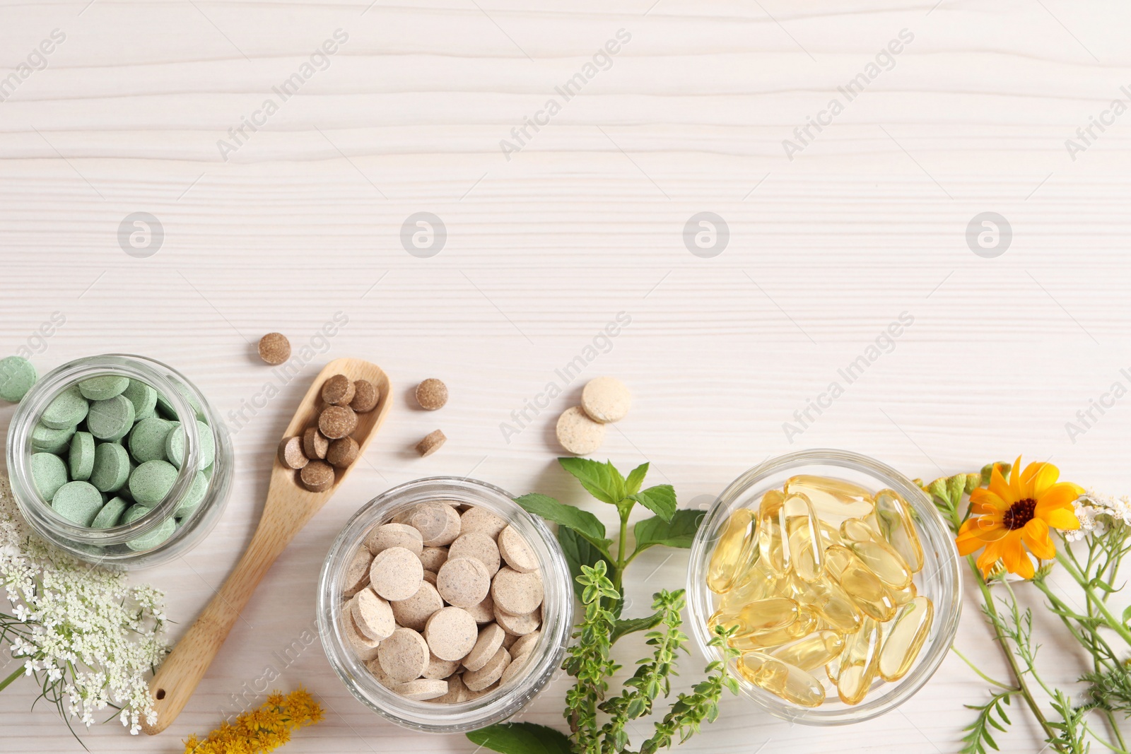 Photo of Different pills, flowers and herbs on white wooden table, flat lay with space for text. Dietary supplements