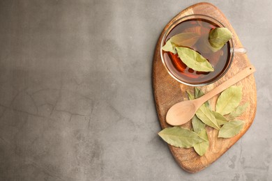 Photo of Cup of freshly brewed tea with bay leaves on grey table, top view. Space for text