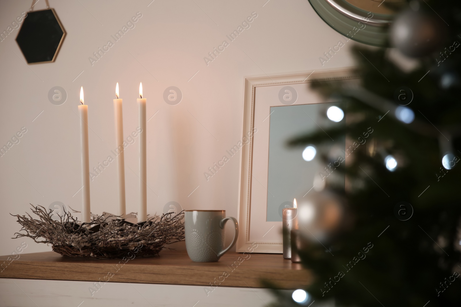 Photo of Burning candles on shelf near Christmas tree indoors