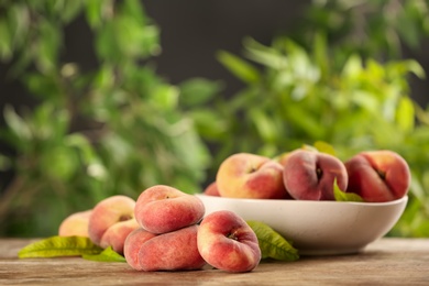 Photo of Fresh ripe donut peaches on wooden table against blurred green background. Space for text
