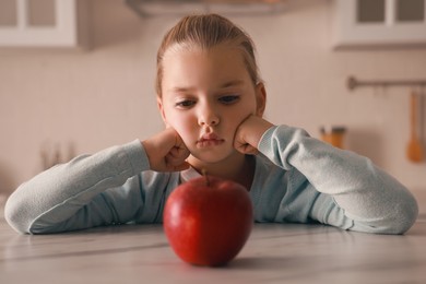 Photo of Cute little girl refusing to eat apple in kitchen