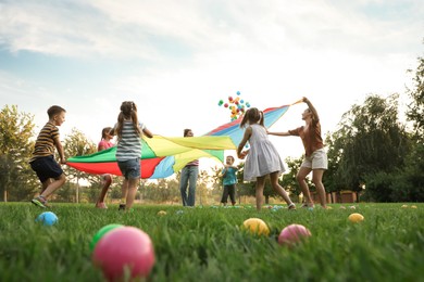 Photo of Group of children and teachers playing with rainbow playground parachute on green grass, low angle view. Summer camp activity