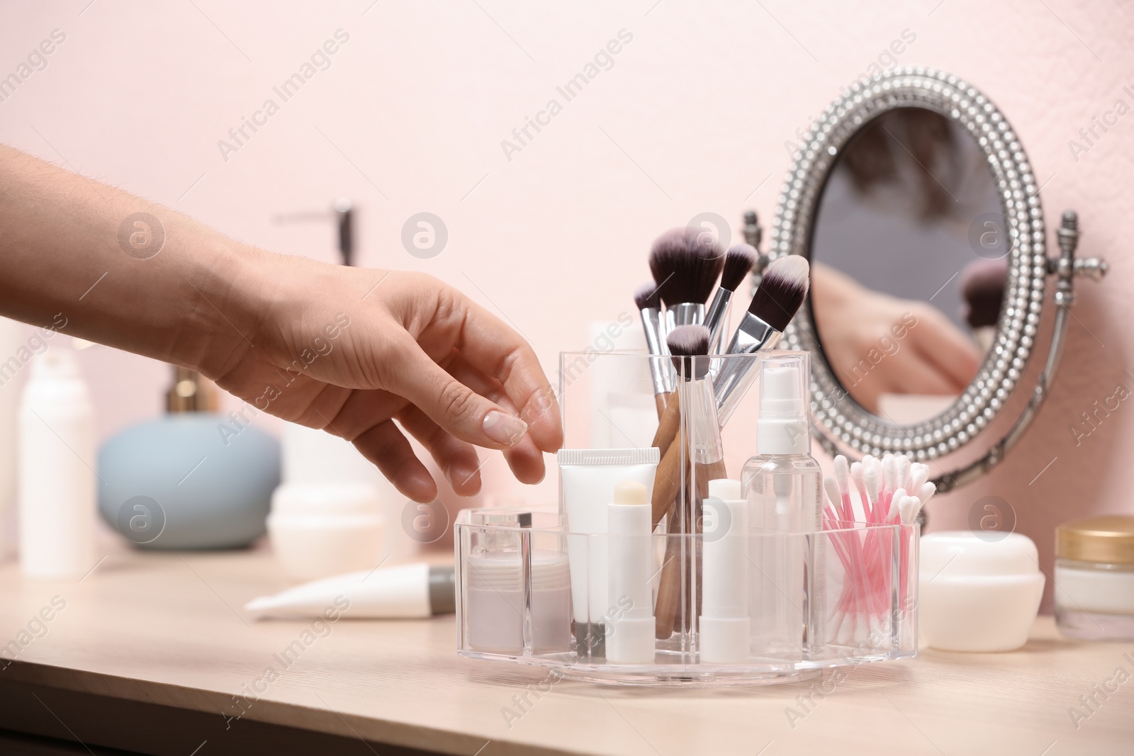 Photo of Woman taking cosmetic products from holder on dressing table, closeup