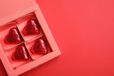 Photo of Tasty chocolate heart shaped candies in pink box on red background, top view. Space for text