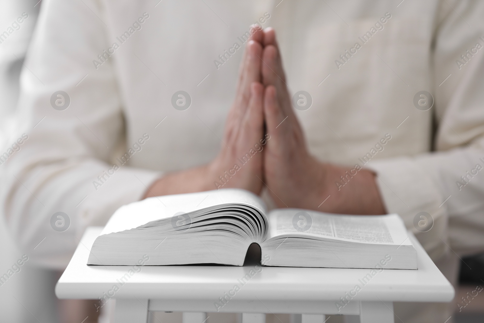 Photo of Religion. Christian man praying over Bible indoors, closeup