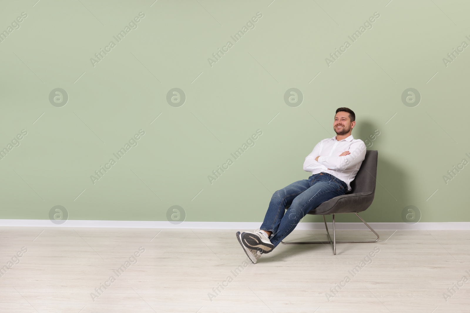 Photo of Happy man sitting in armchair near light green wall indoors, space for text