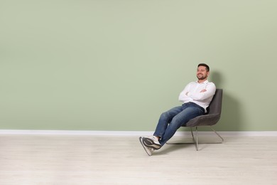 Photo of Happy man sitting in armchair near light green wall indoors, space for text