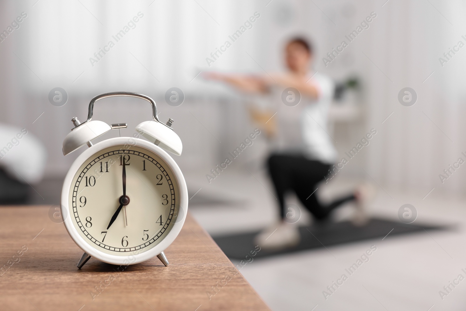 Photo of Morning routine. Alarm clock on wooden table and woman doing exercise, selective focus. Space for text