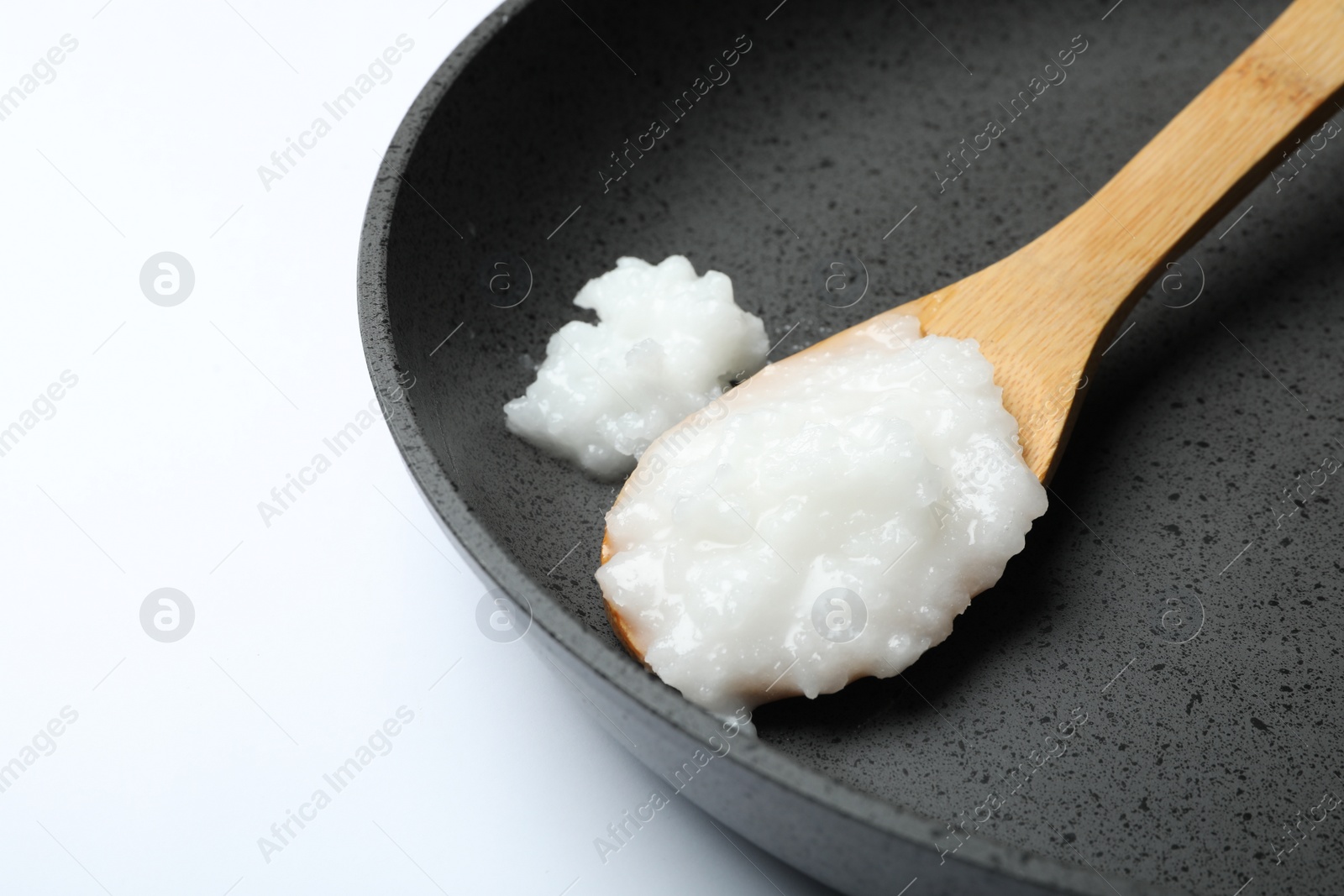 Photo of Frying pan with coconut oil and wooden spoon on white background, closeup. Healthy cooking