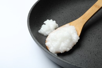 Frying pan with coconut oil and wooden spoon on white background, closeup. Healthy cooking