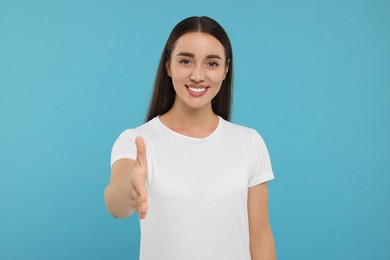Happy young woman welcoming and offering handshake on light blue background