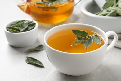 Photo of Cup of sage tea and green leaves on white table