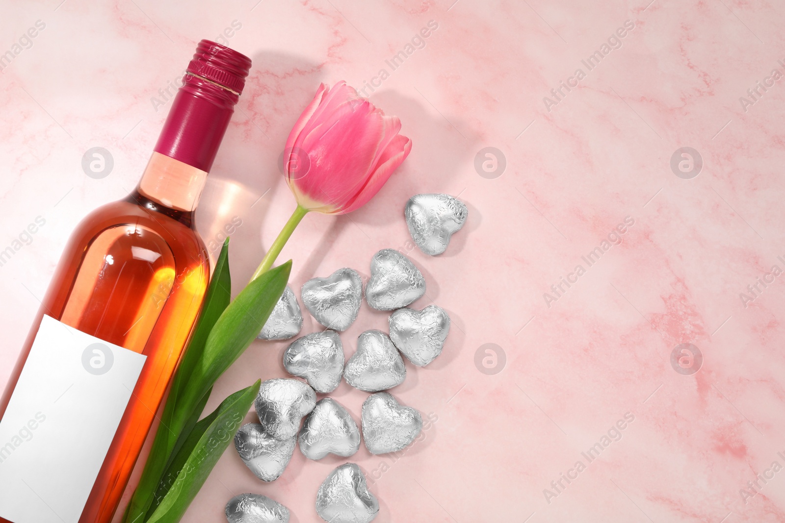Photo of Delicious heart shaped chocolate candies, beautiful tulip and bottle of wine on pink table, flat lay. Space for text