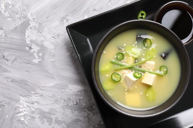 Photo of Bowl of delicious miso soup with tofu on light grey table, top view. Space for text