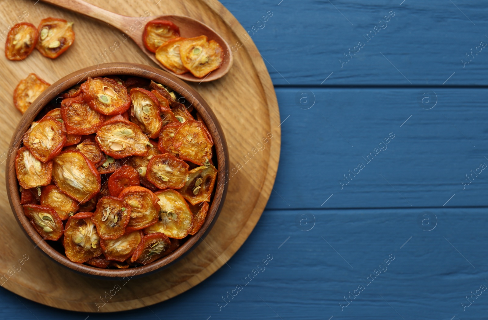 Photo of Bowl and spoon with cut dried kumquat fruits on blue wooden table, top view. Space for text