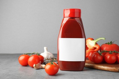 Bottle of tasty ketchup and ingredients on grey table. Space for text