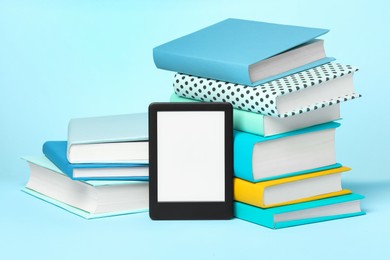 Photo of Modern e-book reader and stacks of hard cover books on light blue background