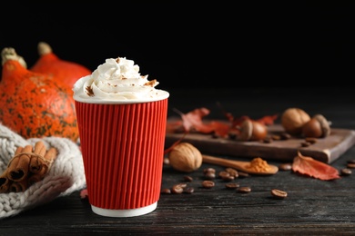 Paper cup with tasty pumpkin spice latte on black wooden table. Space for text