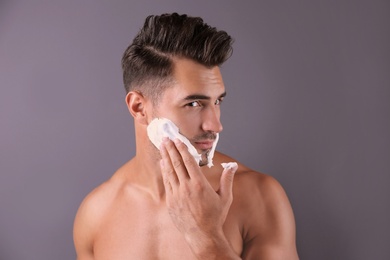 Handsome young man applying shaving foam on color background