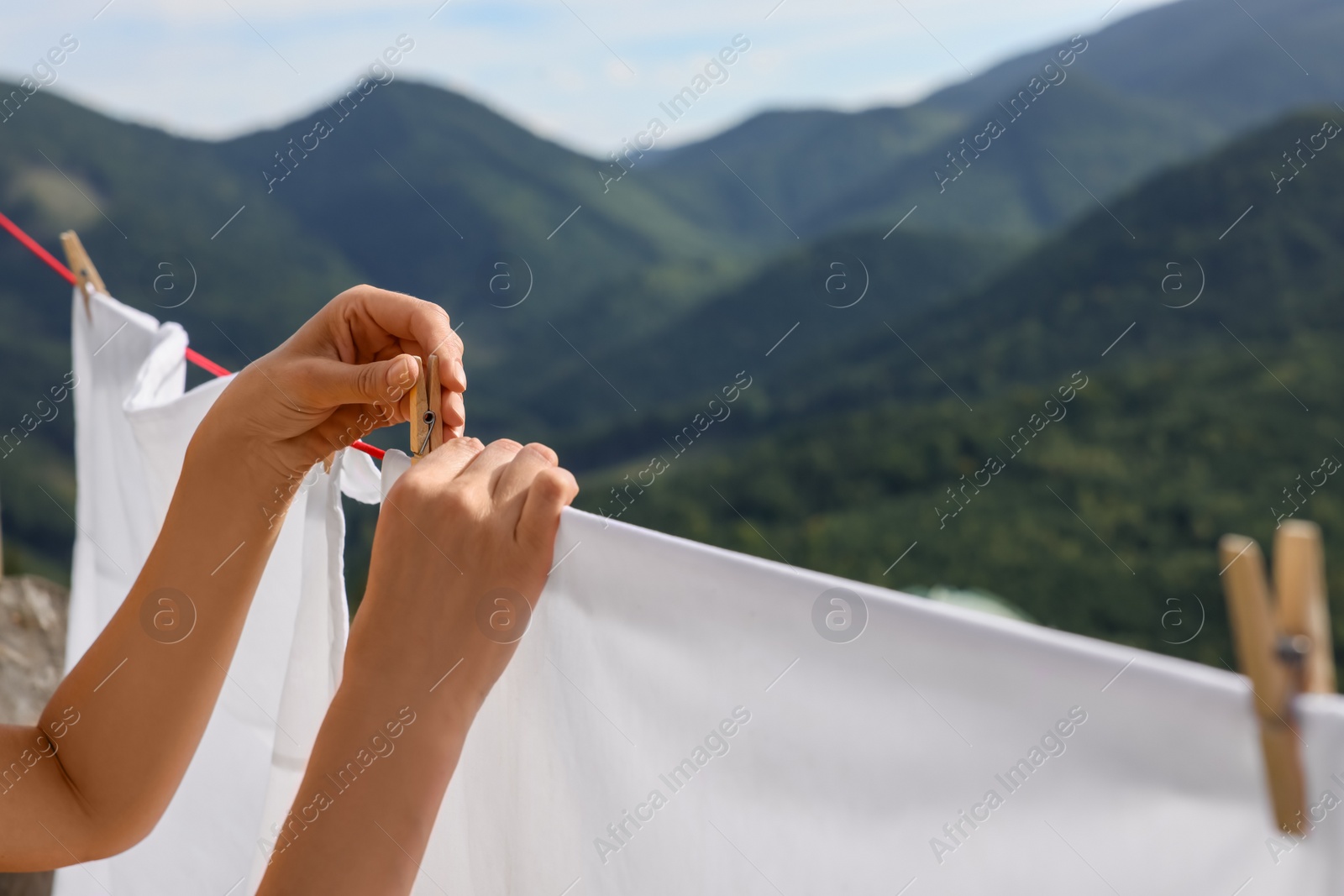 Photo of Woman hanging clean laundry with clothespins on washing line in mountains, closeup. Space for text