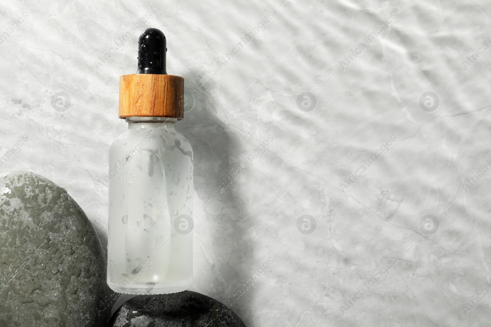 Photo of Bottle of face serum and spa stones in water on light background, flat lay. Space for text