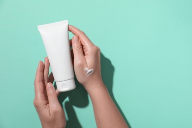 Woman with tube of hand cream on turquoise background, top view. Space for text